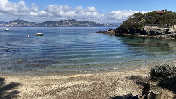 Una playa costera con agua cristalina, barcos y un pueblo lejano.