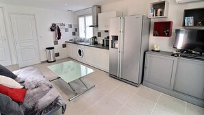 Una cocina moderna con lavadora, un refrigerador grande, un comedor con mesa de vidrio y televisión.