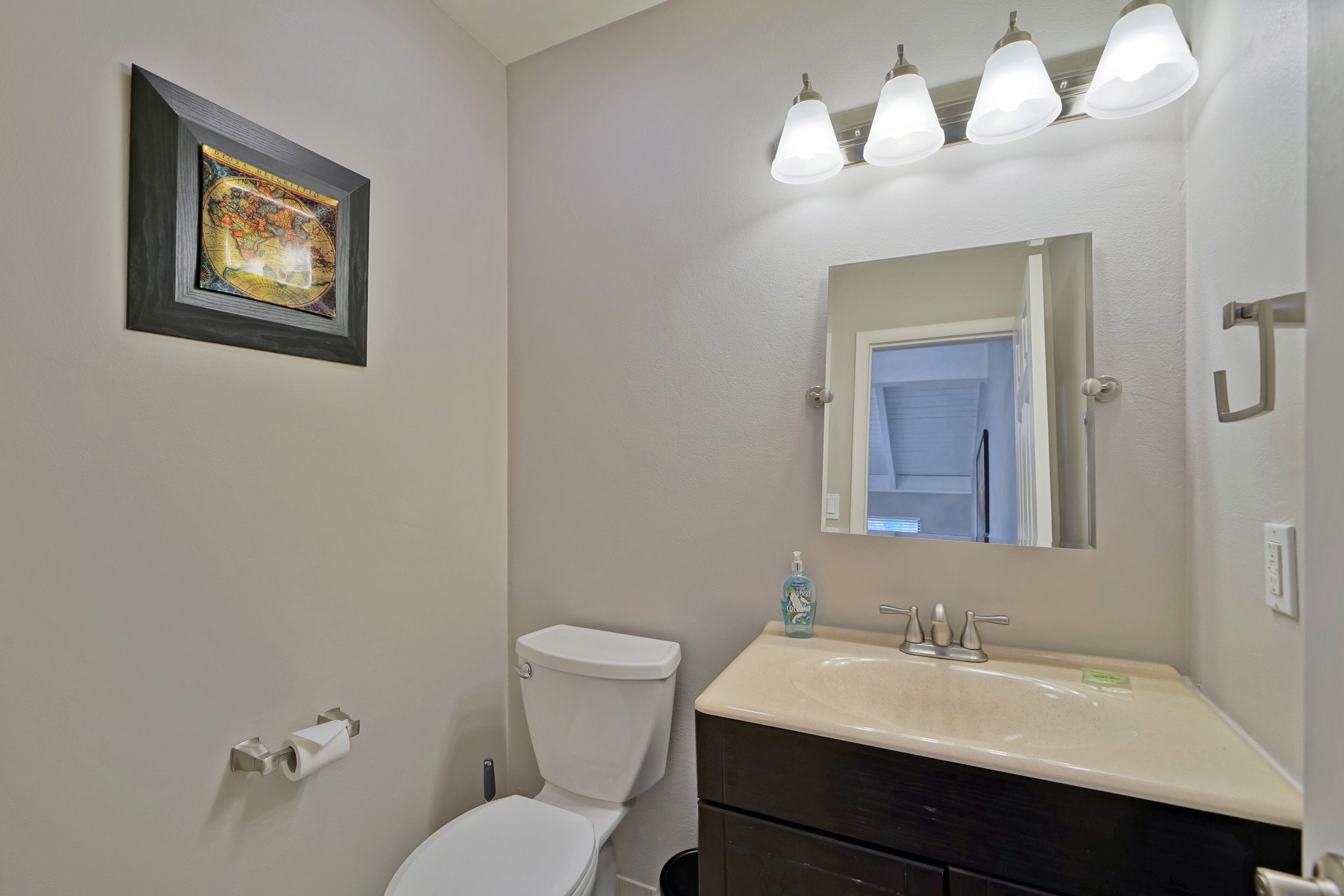 Une salle de bain équipée de toilettes, d’un lavabo, d’un miroir et d’un tableau encadré accroché au mur.