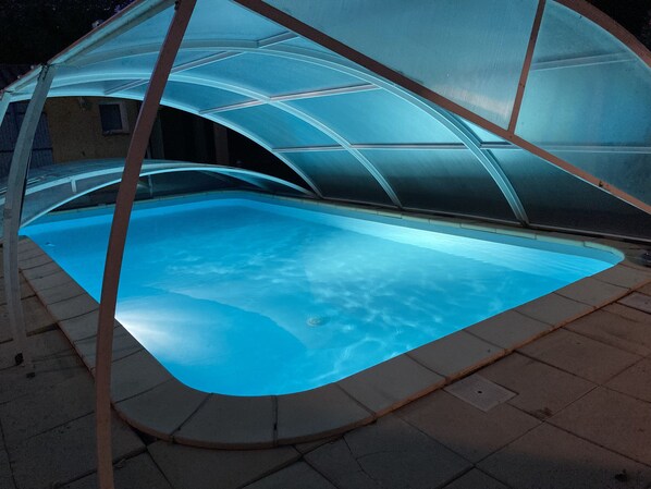 A swimming pool with a glass enclosure, surrounded by a tiled deck.