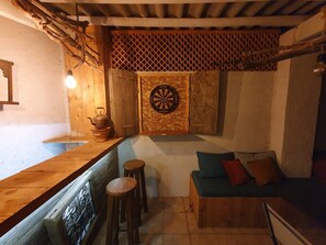 A cozy room with a wooden bench, stools, a dartboard, and a small table with a kettle.