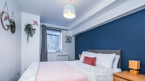 A bedroom with a bed, bedside tables, a window, and a blue accent wall. - Old Town Gem - Castle, Dark History, Uni (Edinburgh)