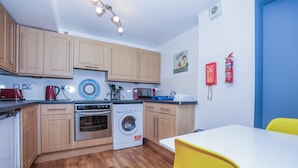 A compact kitchen with wooden cabinets, a microwave, a kettle, and a washing machine. - Old Town Gem - Castle, Dark History, Uni (Edinburgh)