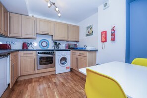 A compact kitchen with wooden cabinets, a microwave, a kettle, and a washing machine. - Old Town Gem - Castle, Dark History, Uni (Edinburgh)