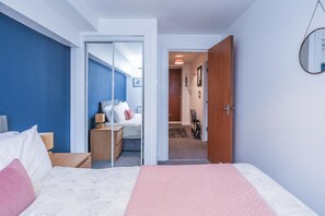 Ein Schlafzimmer mit einem Bett, Nachttischen, einem Kleiderschrank und einem Spiegel an der Wand.