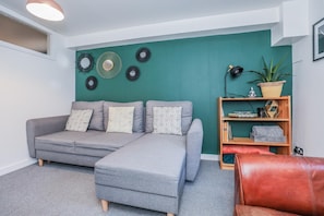 A living room with a grey sectional sofa, a wooden bookshelf, and a red leather chair.