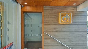 Una entrada moderna a un edificio con techo de madera, puerta de cristal y un letrero con las letras "d i" iluminadas.