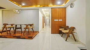 Un vestíbulo de hotel con un mostrador de recepción de madera, sillas, un reloj y suelo de baldosas.