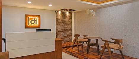 A reception area with a wooden reception desk, a stone wall, a round table with chairs, and a ceiling fan.