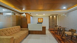 Zona de recepción con sofá, mostrador de recepción y comedor con suelo de madera y sillas.