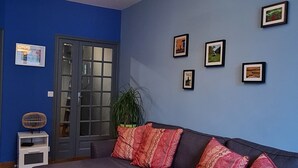 Una sala de estar con sofá modular, piso de madera, pared azul y lámpara colgante.