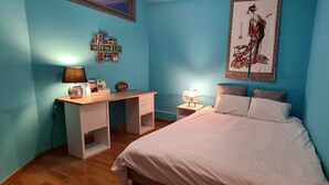 Un dormitorio con cama, escritorio, mesita de noche y una obra de arte en la pared.
