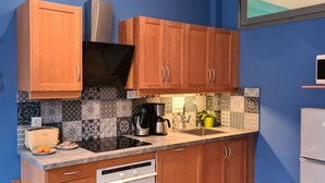 Cocina compacta con armarios de madera, encimera negra y varios electrodomésticos, incluyendo cafetera, tostadora y microondas.