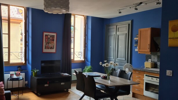 Un espacio habitable compacto con zona de comedor, kitchenette y televisor sobre un soporte.