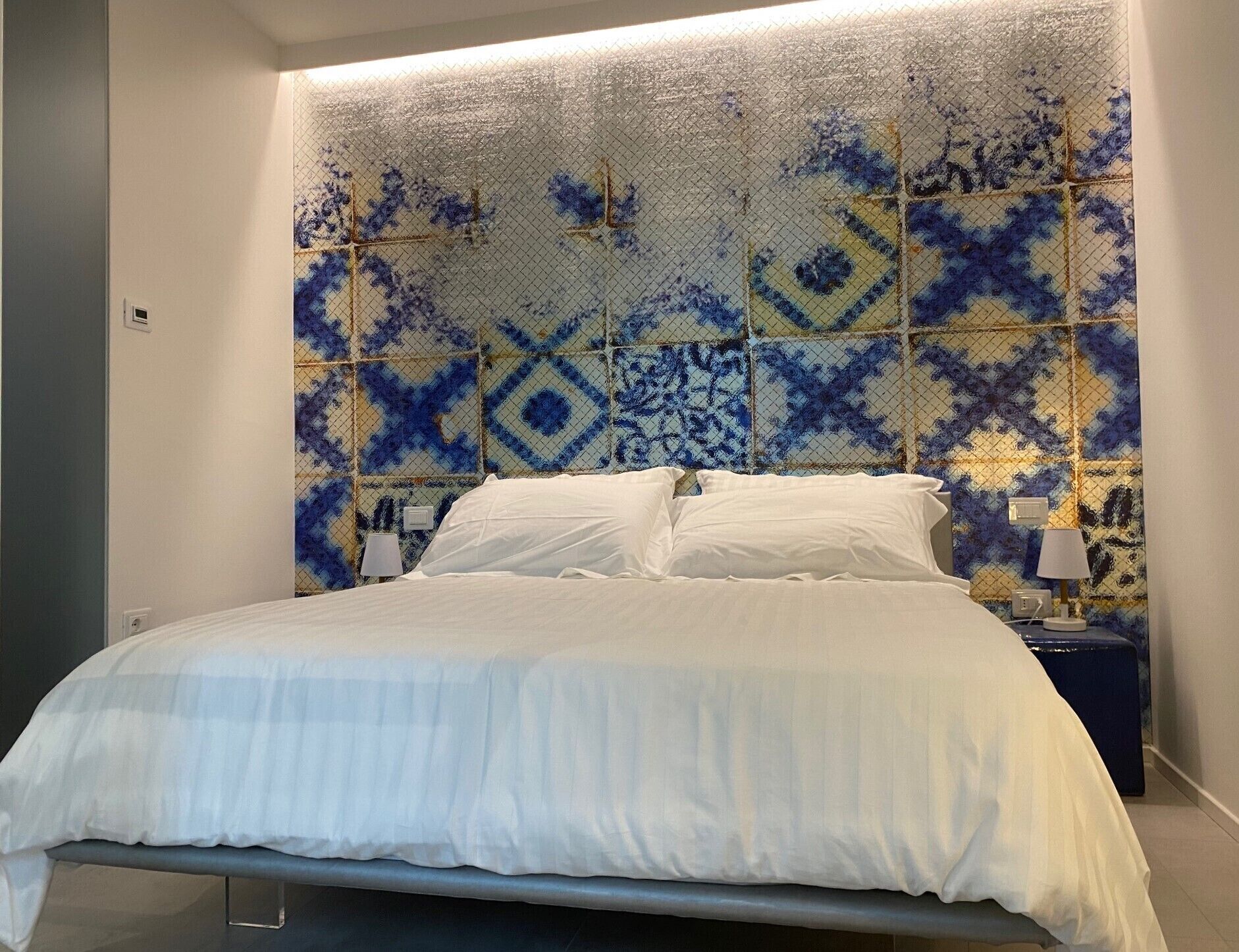 Une chambre à coucher avec un lit, une table de chevet et un mur orné de carreaux décoratifs.