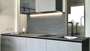 A modern kitchen with a large island, built-in appliances, and a window providing a view. - Maisonette (Tenno)