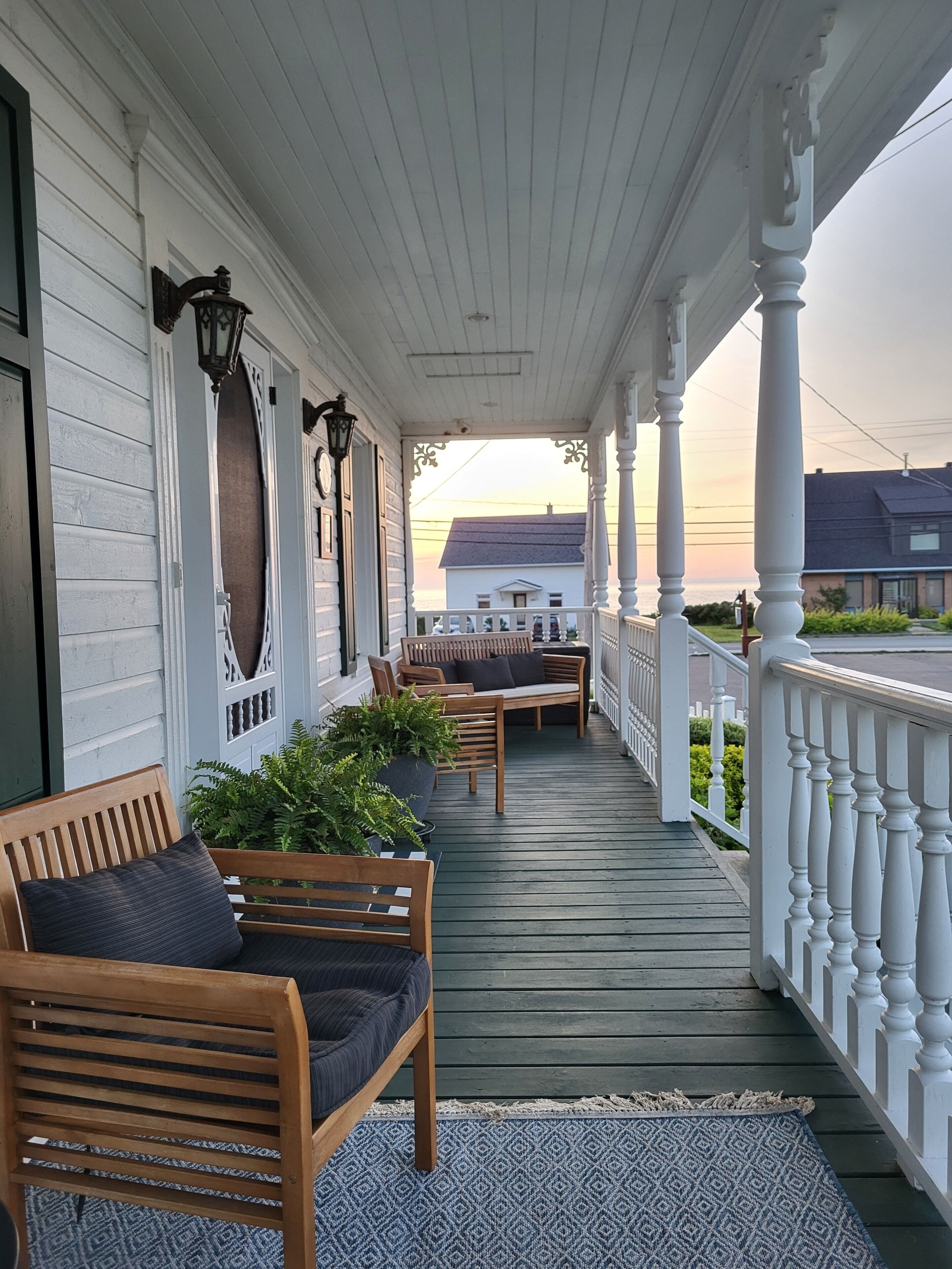 A covered porch with wooden furniture, a railing, and a view of the sunset.