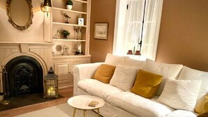 A cozy living room with a white sofa, a small round table, a fireplace, and decorative shelves. - LA BELLE BLANCHE MAISON VUE DU FLEUVE, PRÈS DE MÉTIS SUR MER (Saint-Ulric)