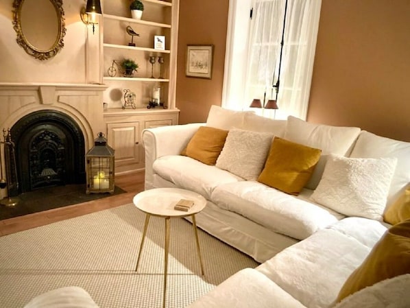 A cozy living room with a white sofa, a small round table, a fireplace, and decorative shelves. - LA BELLE BLANCHE MAISON VUE DU FLEUVE, PRÈS DE MÉTIS SUR MER (Saint-Ulric)