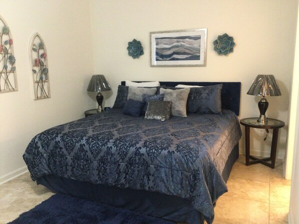 A bedroom with a large bed, two bedside tables, a wall-mounted lamp, and a framed picture.
