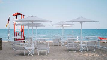 Une plage avec des chaises longues blanches et des parasols, une tour de surveillance pour les sauveteurs et un drapeau.