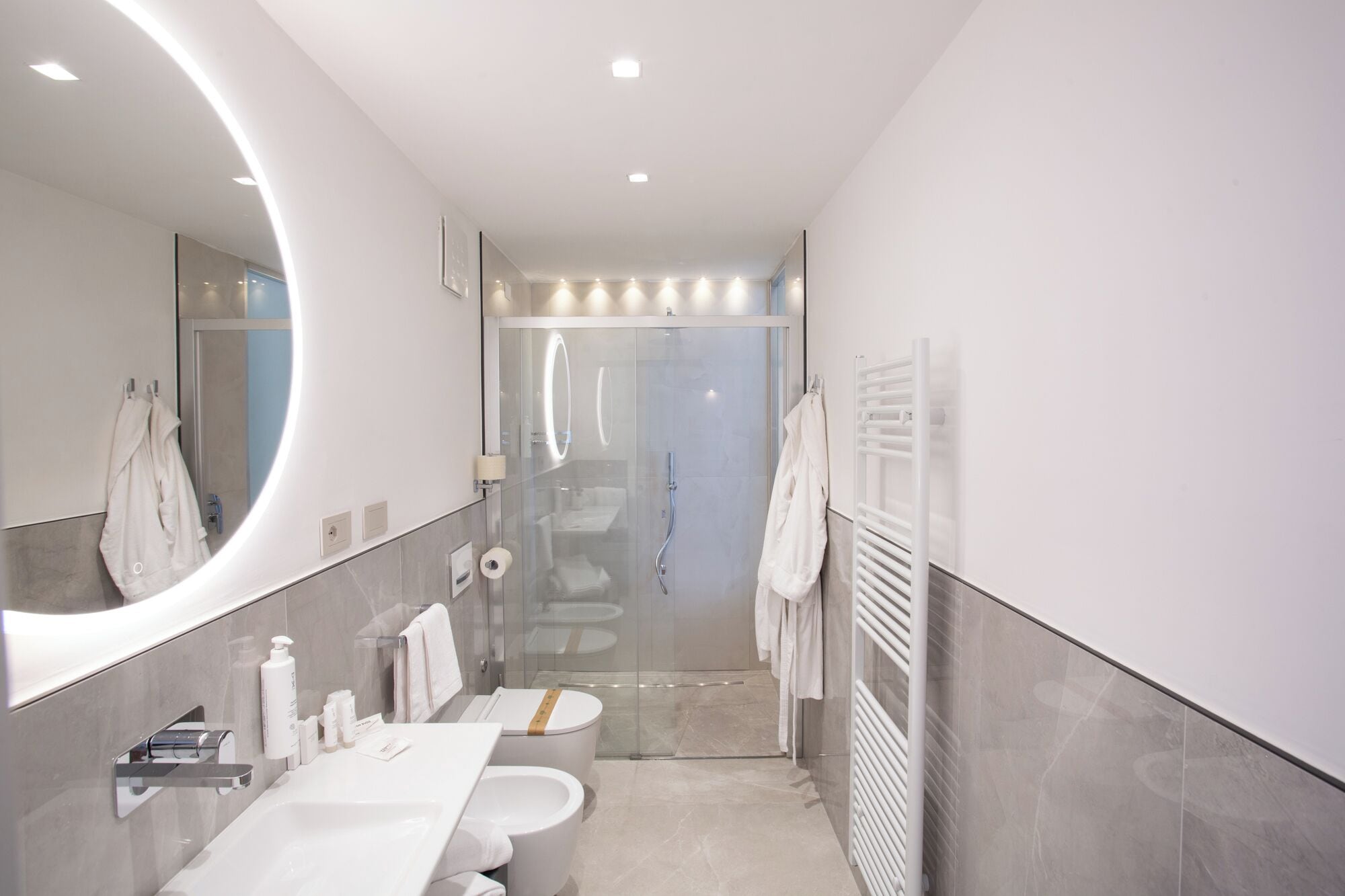 Un bagno moderno con uno specchio grande, cabina doccia in vetro, lavandino bianco e porta asciugamani.