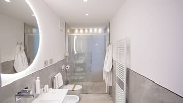 Un bagno moderno con uno specchio grande, cabina doccia in vetro, lavandino bianco e porta asciugamani.