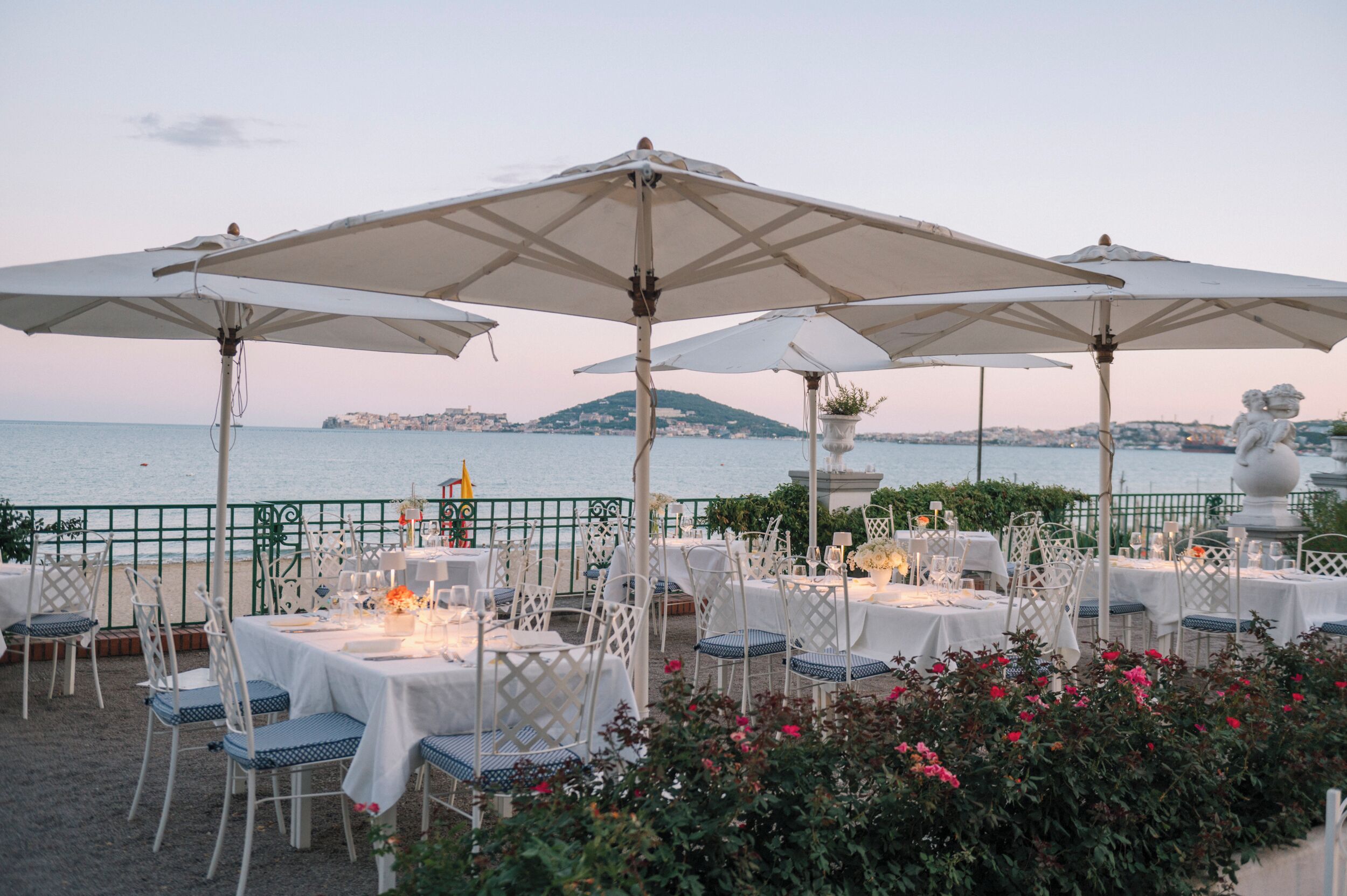 Un espacio de comedor al aire libre con mesas y sillas, sombrillas y vista al mar.