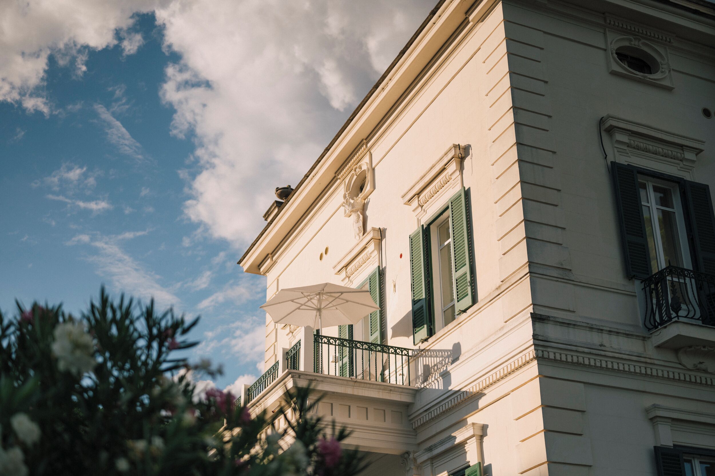 Un edificio con un balcone, una facciata bianca e persiane verdi.