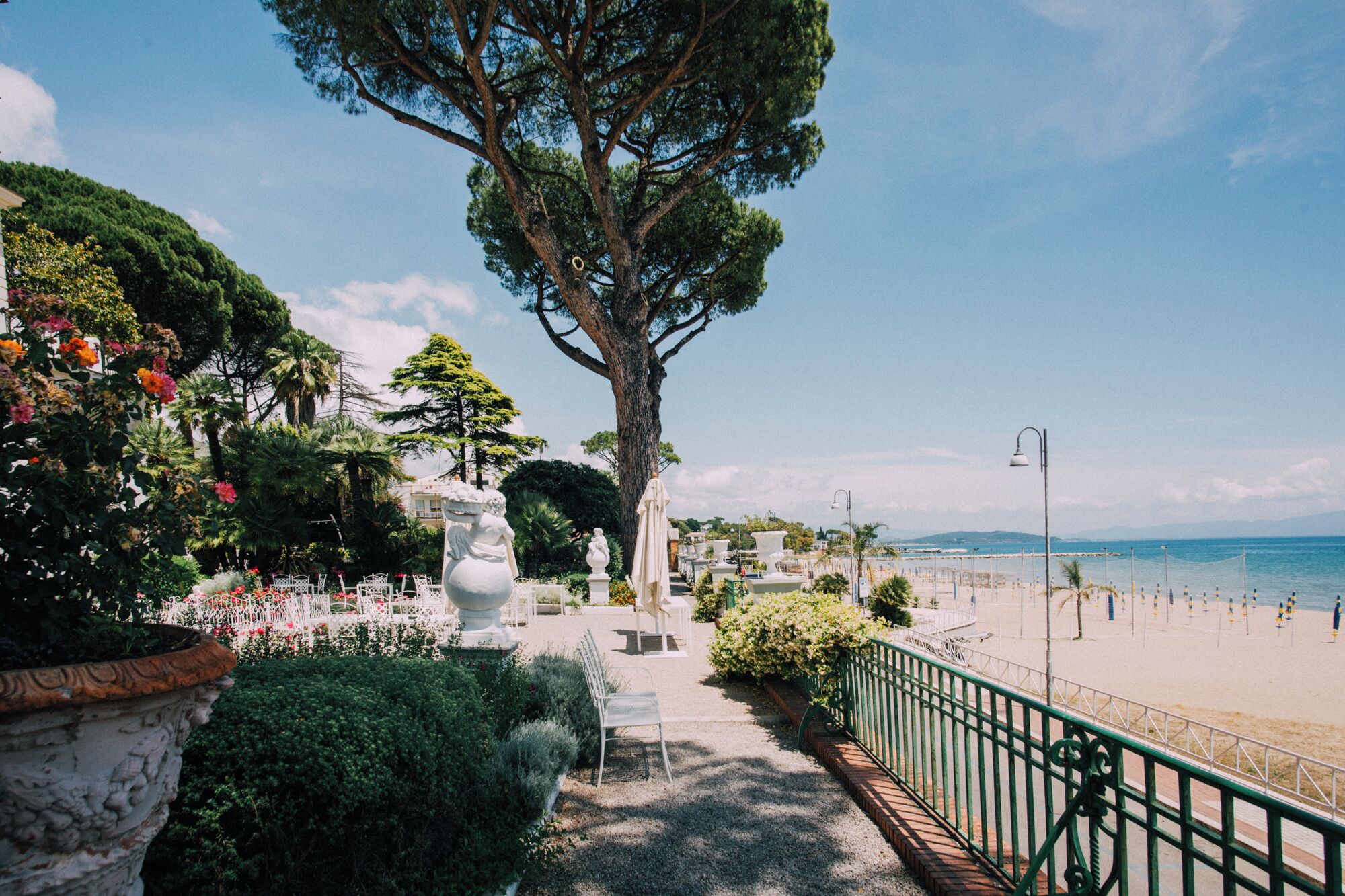A pathway leading to a beach with a railing, trees, and outdoor seating.
