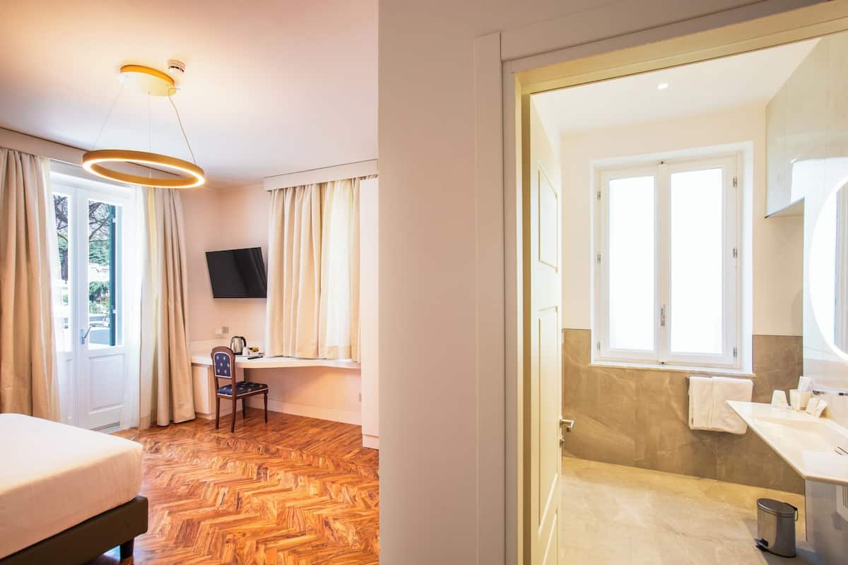 Hotellihuoneessa on puinen kalanruotokuvioinen lattia, sänky, työpöytä tuolilla, seinälle asennettu televisio sekä kylpyhuone, jossa on pesuallas ja peili.