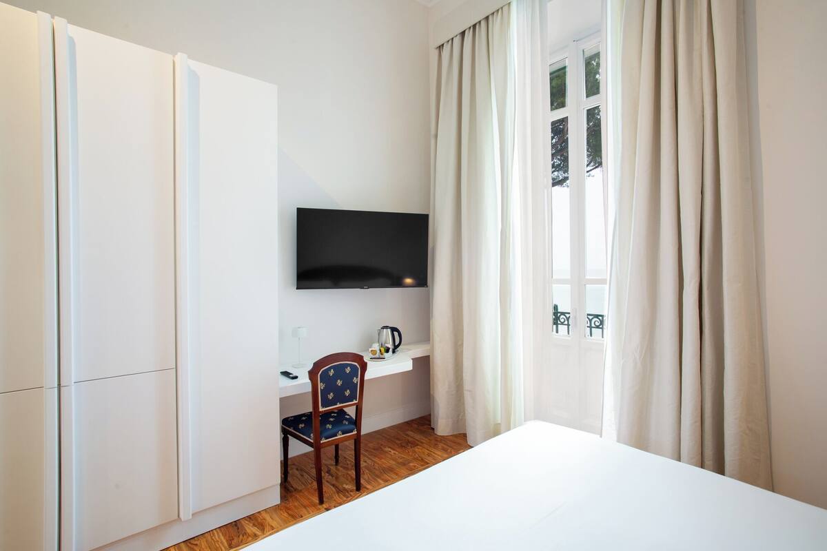 Hotellihuone, jossa on sänky, työpöytä tuolilla, seinälle asennettu televisio ja ikkuna, jossa on verhot.