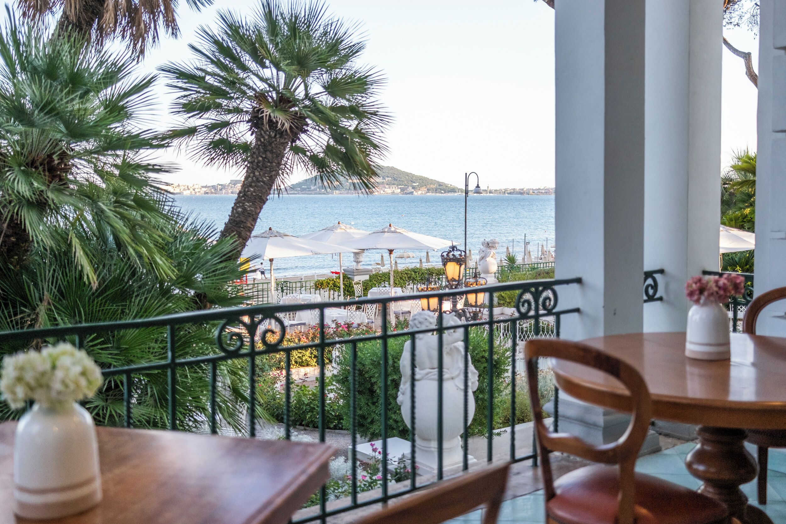 Ein Balkon mit Meerblick, ein Tisch mit einer Vase und eine Statue.