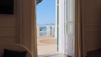 Eine geöffnete Tür, die auf einen Balkon mit Blick auf das Meer und eine entfernte Stadt führt.