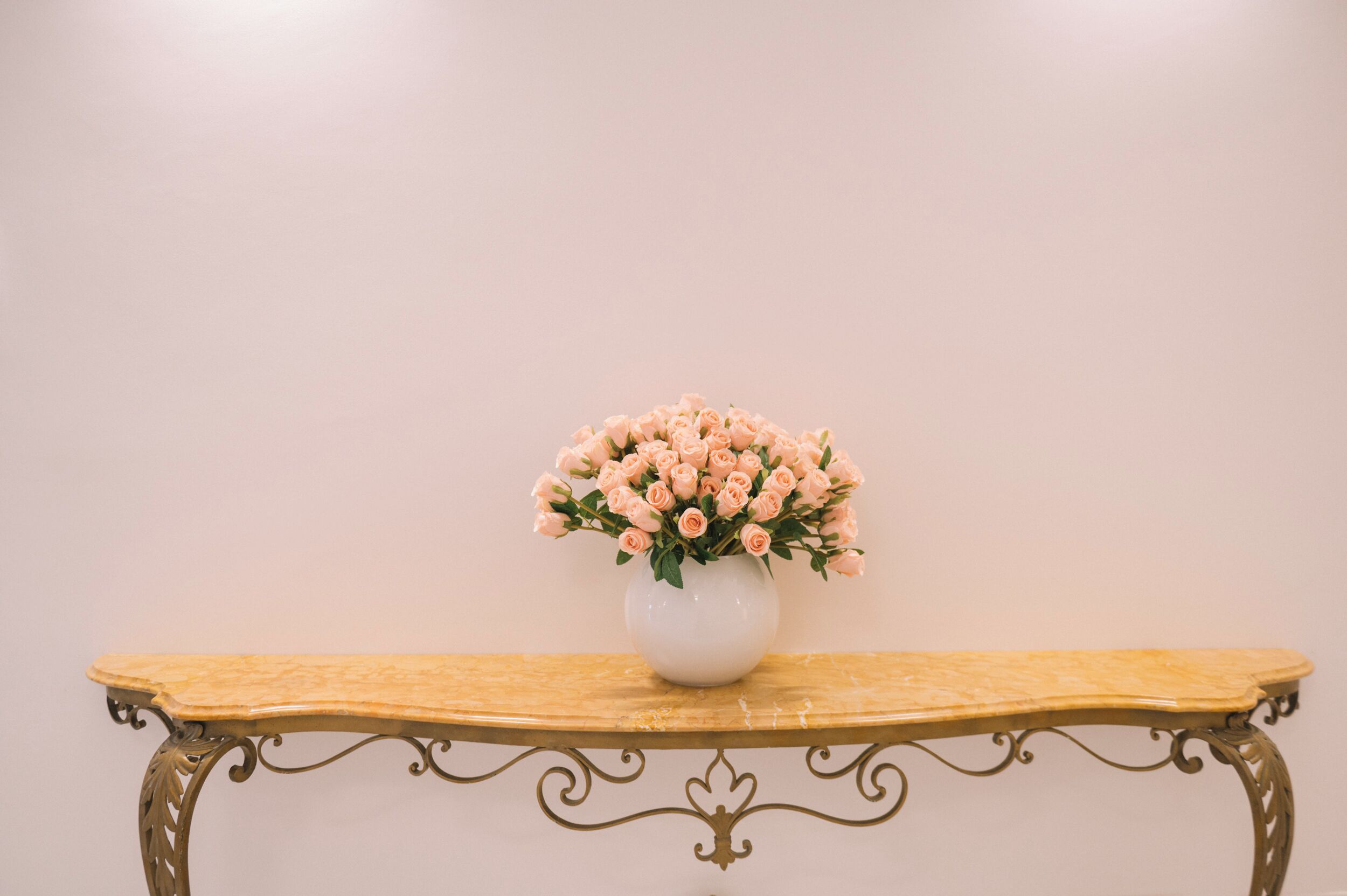 Un vaso bianco con fiori rosa su un tavolo di legno, su uno sfondo neutro.
