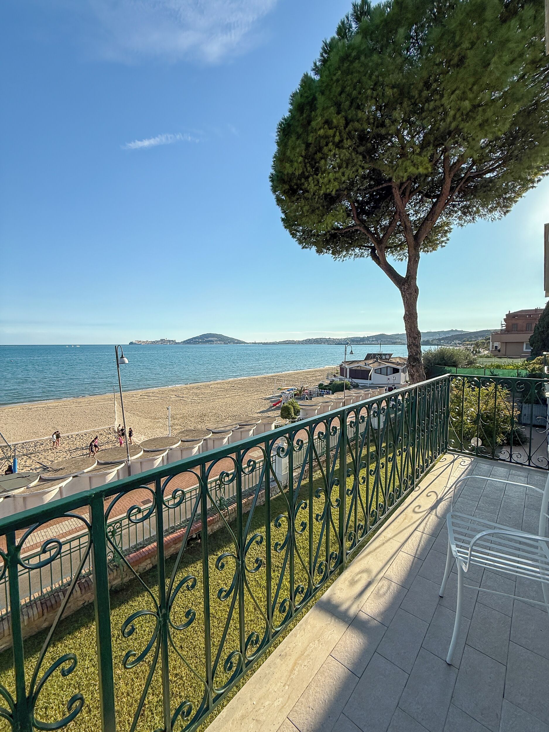 A balcony with a view of a beach, a tree, and a clear sky.
