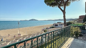 A balcony with a view of a beach, a tree, and a clear sky.