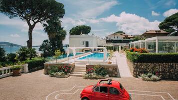 Un'auto rossa parcheggiata di fronte a una zona piscina, con un edificio bianco sullo sfondo.