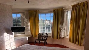 Une chambre à coucher comprenant un lit, une chaise, un bureau avec une télévision et des fenêtres avec des rideaux.