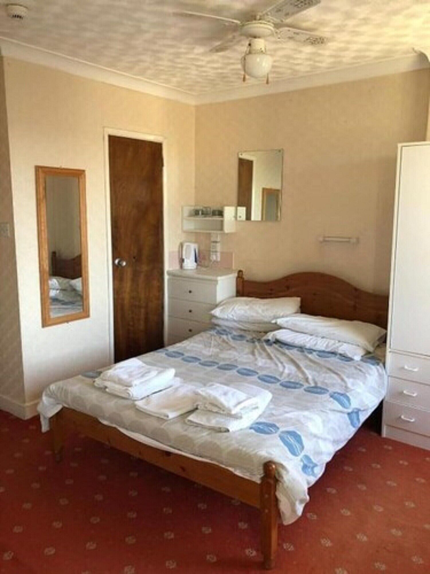 A bedroom with a bed, a wardrobe, a mirror, and a ceiling fan.