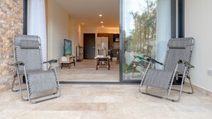 A modern living room with a large sliding glass door leading to a dining area. There are two grey folding chairs in the foreground. - Condo Verde Oasis -  Veranto Condos (Playa del Carmen)