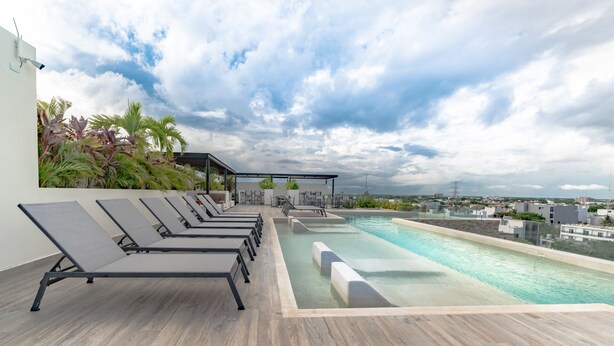 A rooftop pool area with lounge chairs, a pool, and a view of the cityscape. - Condo Verde Oasis -  Veranto Condos (Playa del Carmen)