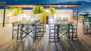 An outdoor dining area with wooden tables and chairs, surrounded by plants and a glass railing. - Condo Verde Oasis -  Veranto Condos (Playa del Carmen)