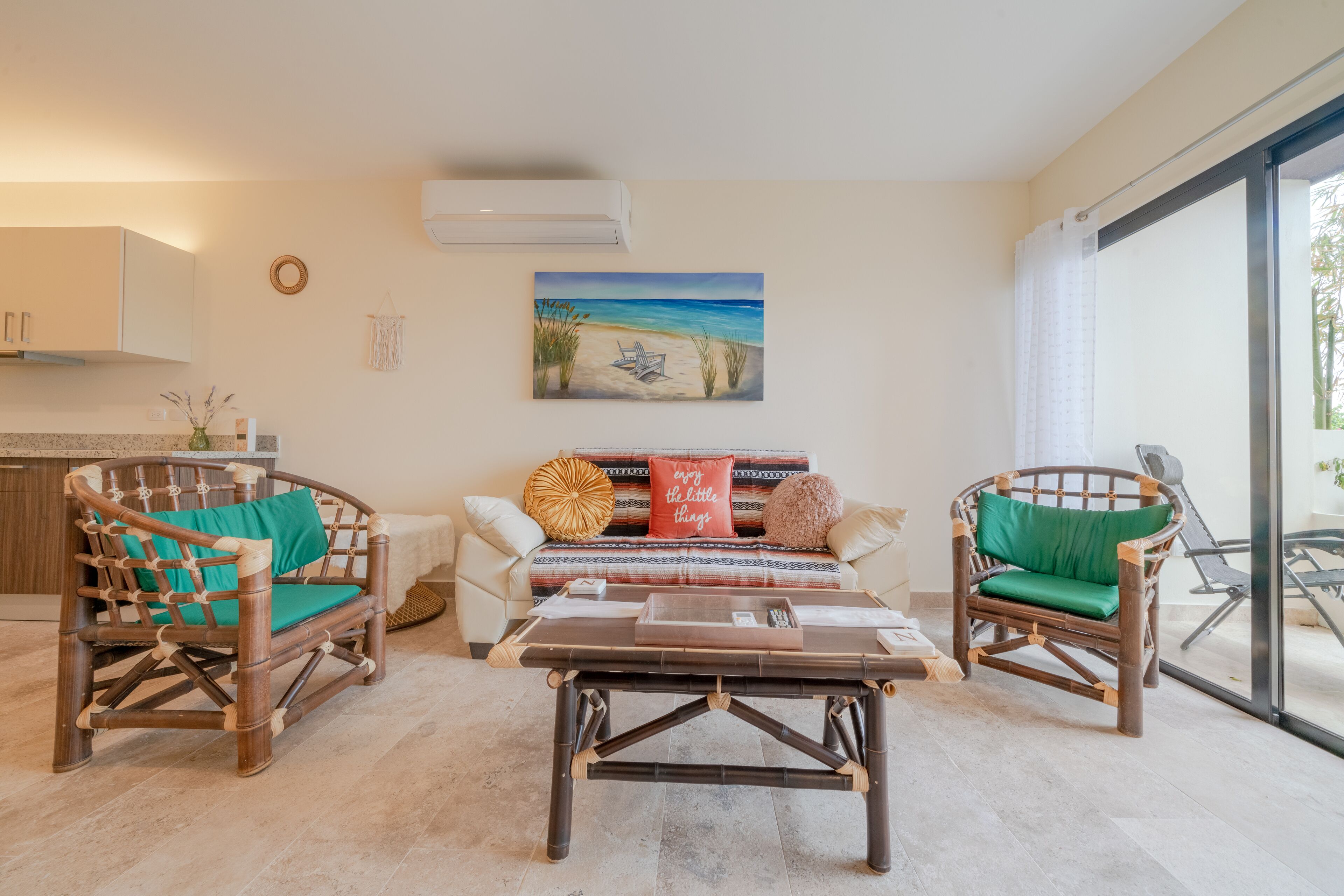 A living room with a sofa, two wicker chairs, a coffee table, and a painting of a beach scene.