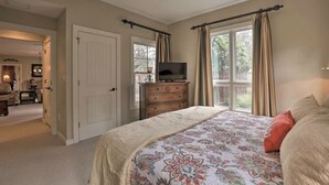 Une chambre à coucher avec un grand lit, une commode, un téléviseur et une fenêtre avec des rideaux.