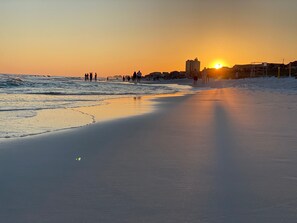 A beach at sunset with people walking along the shore.