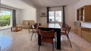 En rummelig opholdsstue med spisebord, stole, sofa og et køkkenområde med skabe.
