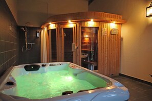 Ein Whirlpool mit Holzumrandung, einer Duschkabine und einer Wandleuchte.