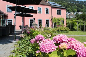 Ein pinkfarbenes Gebäude mit einer Terrasse, Sitzgelegenheiten im Freien und einem Garten mit rosa Blumen.