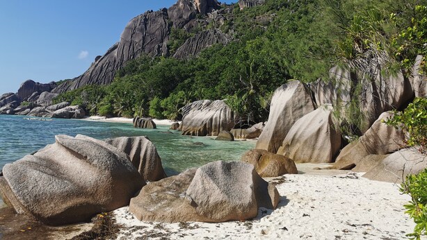 Una playa con grandes rocas, agua turquesa cristalina y un acantilado rocoso con vegetación.
